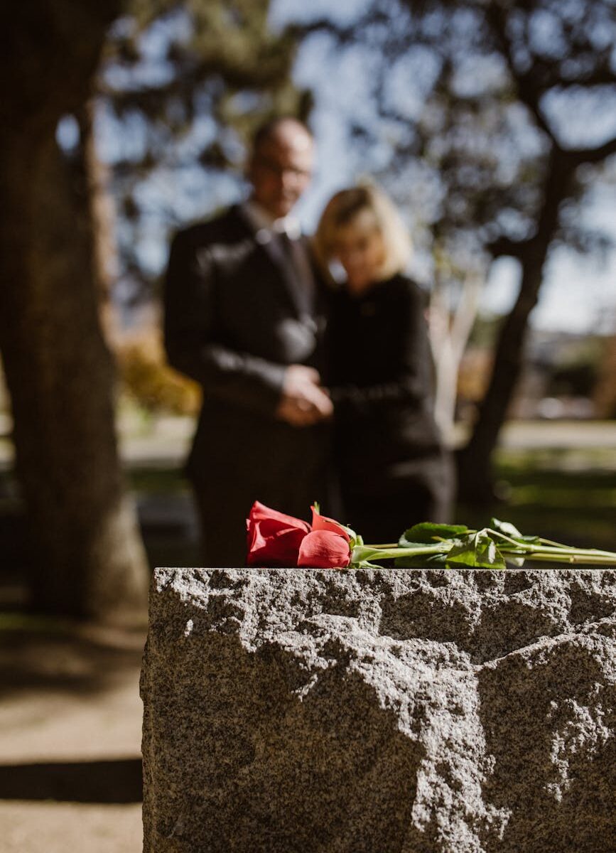 man and woman standing on grave with flower on tombstone