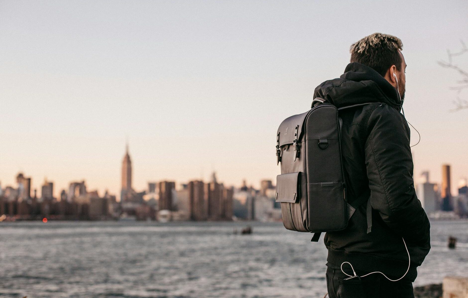man wearing black bubble jacket and black leather backpack near bay