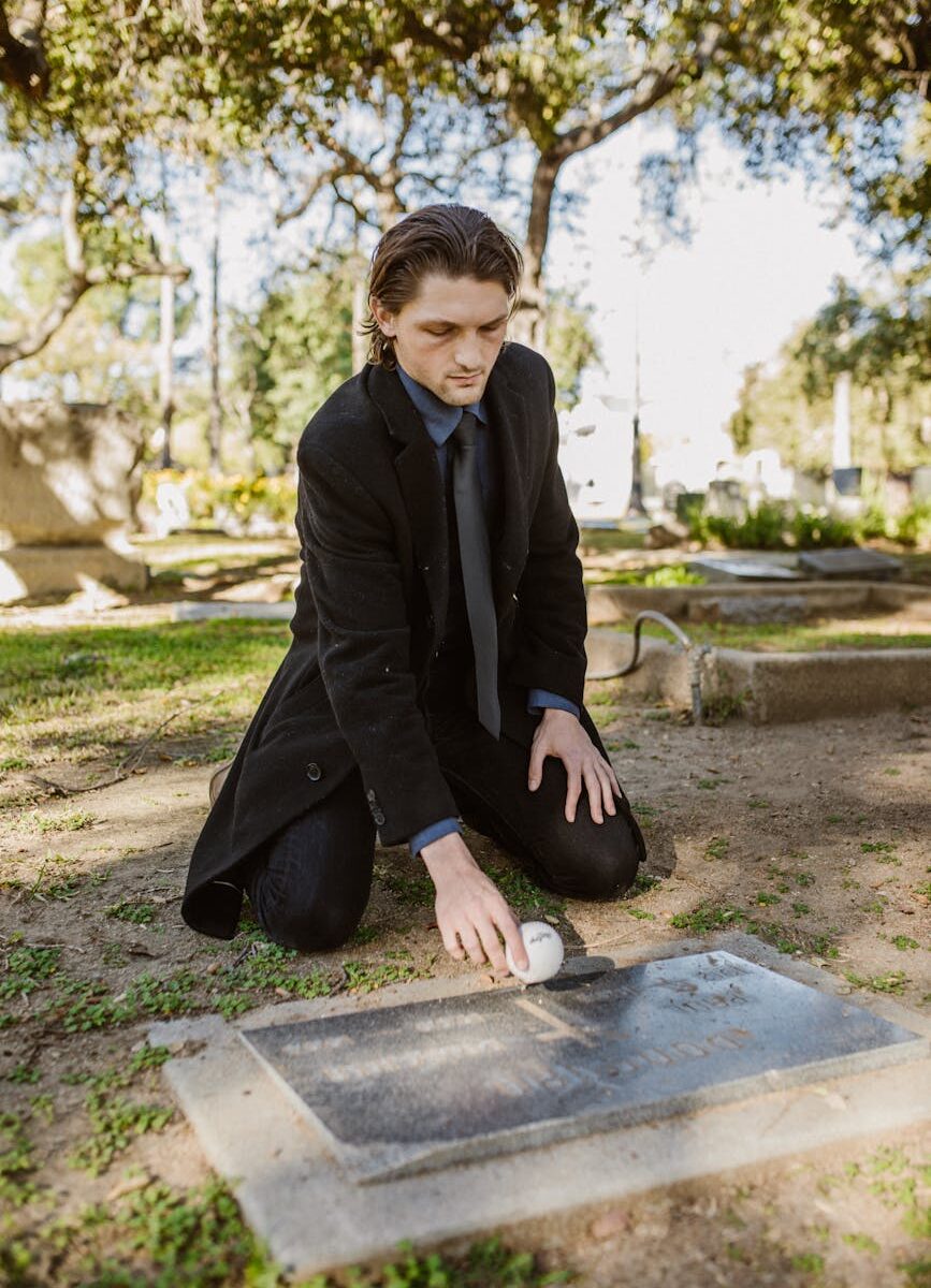 a sad man in black coat putting a ball on the gravestone